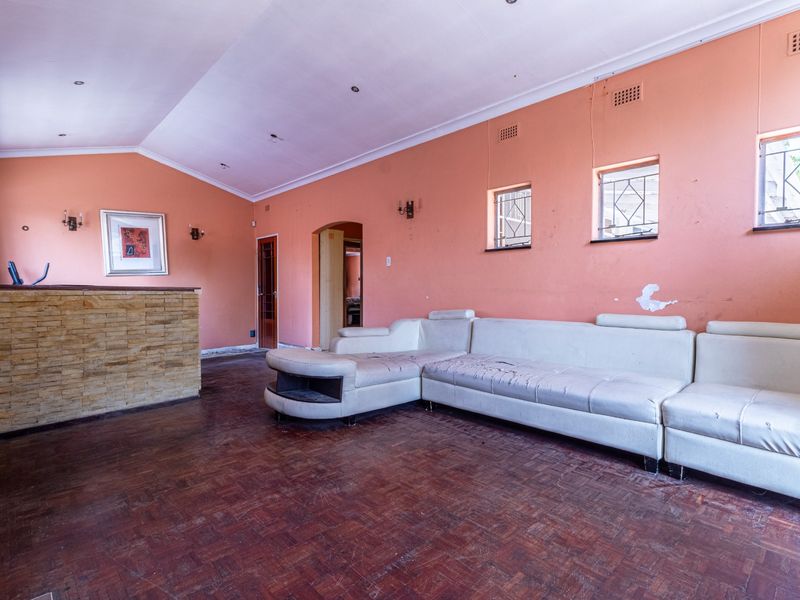 Spacious living room featuring parquet flooring, a stone-clad feature wall, and coved ceilings, offering a blank canvas for renovation and modernization.