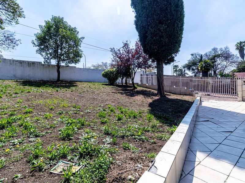 A spacious rear garden area featuring a tiled patio section, perimeter walling, and established trees, offering potential for landscaping and outdoor improvement.