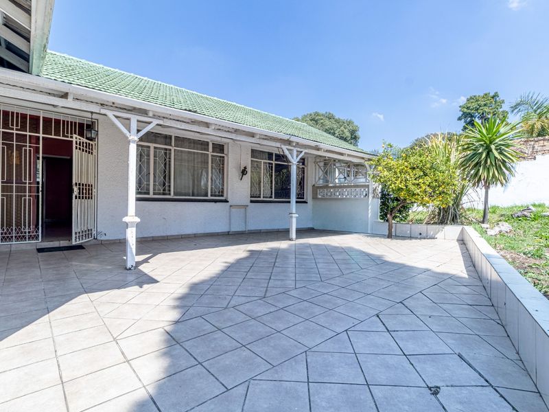 A spacious covered patio area featuring tiled flooring, security gates, and direct access to the rear garden and exterior of the home.