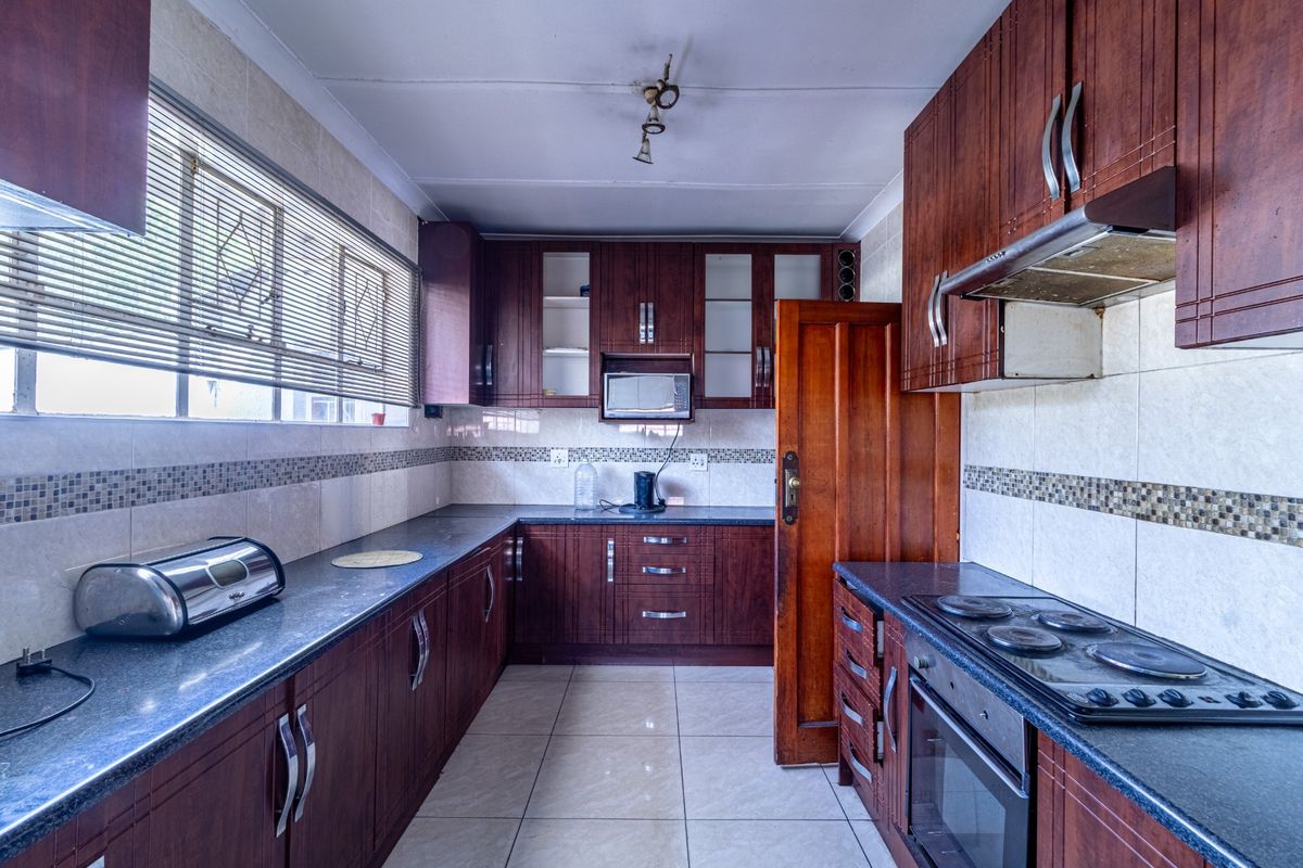 A functional kitchen featuring dark wood cabinetry, granite countertops, a built-in oven, electric hob, and tiled finishes throughout.