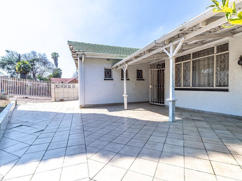 A covered outdoor patio area featuring tiled flooring, security gates, and a veranda structure, providing a functional space for outdoor living.