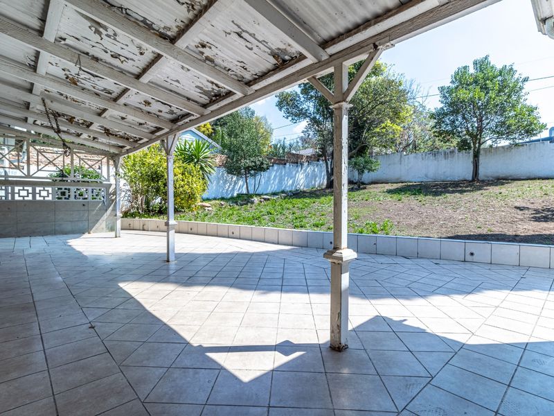 A spacious covered patio featuring tiled flooring, decorative breeze block walling, and a garden view, requiring some maintenance to the ceiling and support columns.