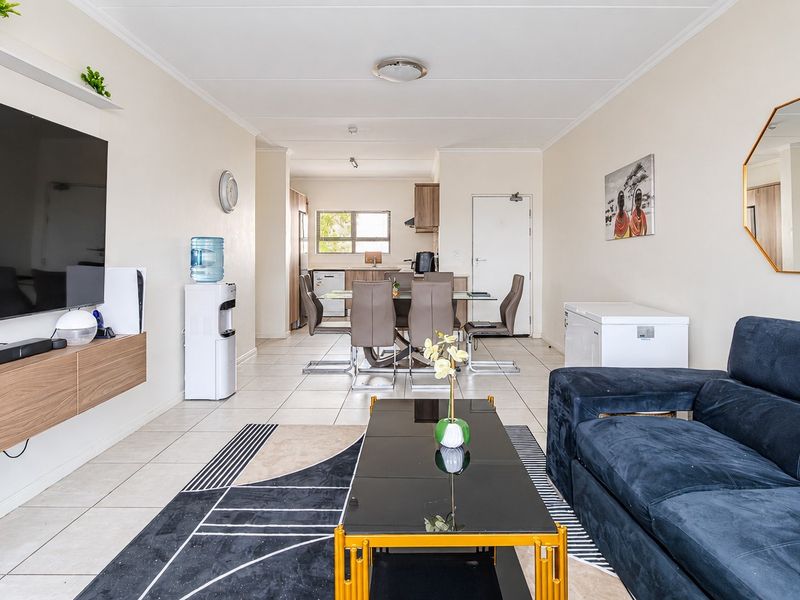 An open-plan living and dining area featuring tiled floors, a modern floating media console, and a functional kitchen space with cabinetry.