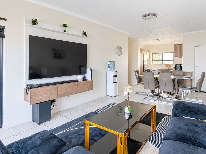 Spacious open-plan living and dining area featuring tiled floors, a modern built-in media console, and an integrated kitchen layout.