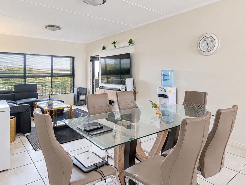 An open-plan living and dining area featuring tiled flooring, large windows for natural light, and a wall-mounted air conditioning unit.