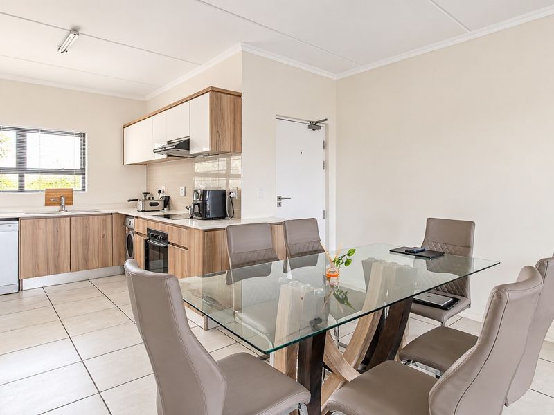 Modern open-plan kitchen and dining area featuring contemporary wood-finish cabinetry, integrated appliances, tiled flooring, and a bright, functional layout.