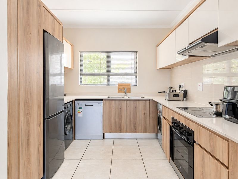 Modern kitchen featuring wood-grain cabinetry, stone countertops, integrated appliances, and tiled flooring, offering a clean and functional workspace.