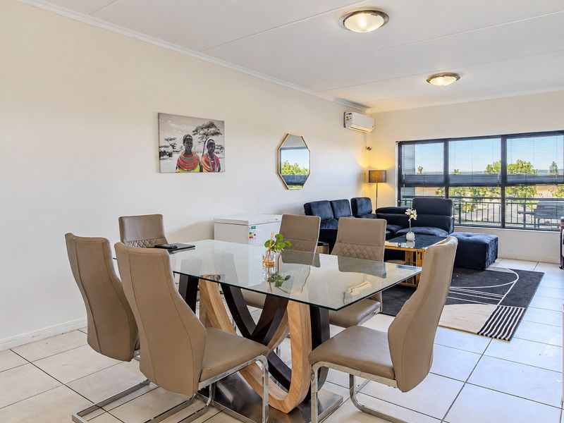 An open-plan living and dining area featuring tiled flooring, large windows providing natural light, and a wall-mounted air conditioning unit.