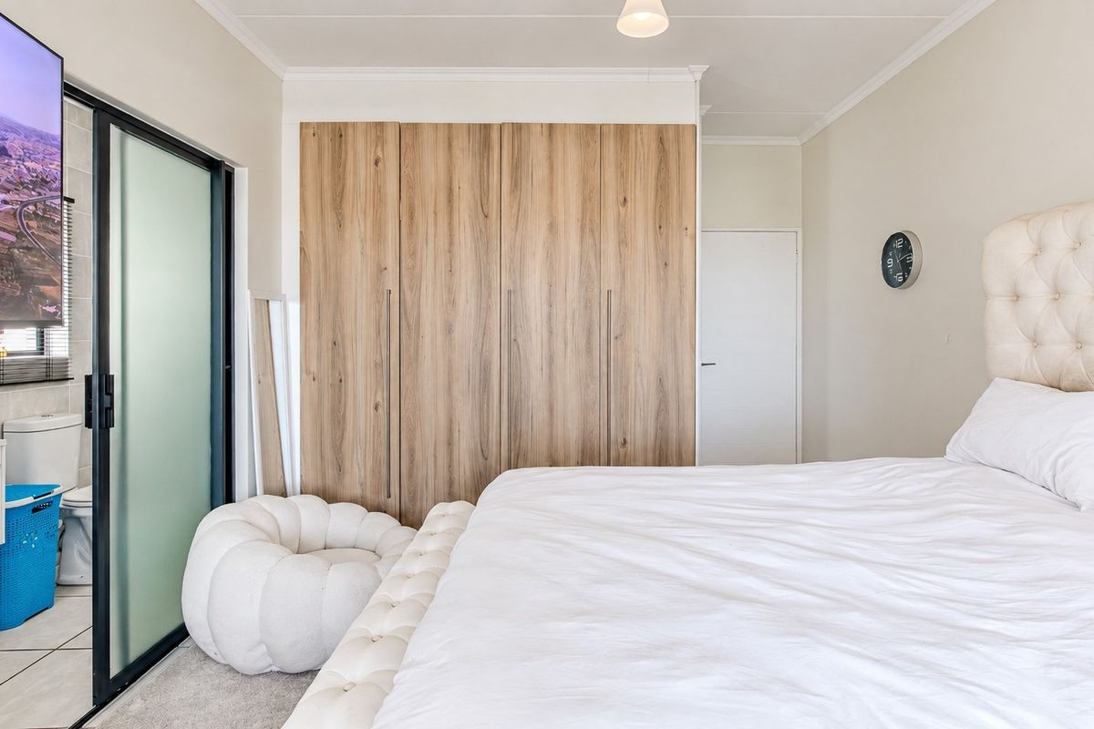 A well-maintained bedroom featuring modern wood-finish built-in cupboards and a sliding glass door providing access to an en-suite bathroom.