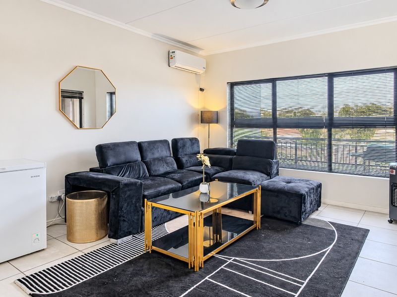 A bright and well-maintained living room featuring tiled flooring, a split-system air conditioner, and a large window with fitted blinds.