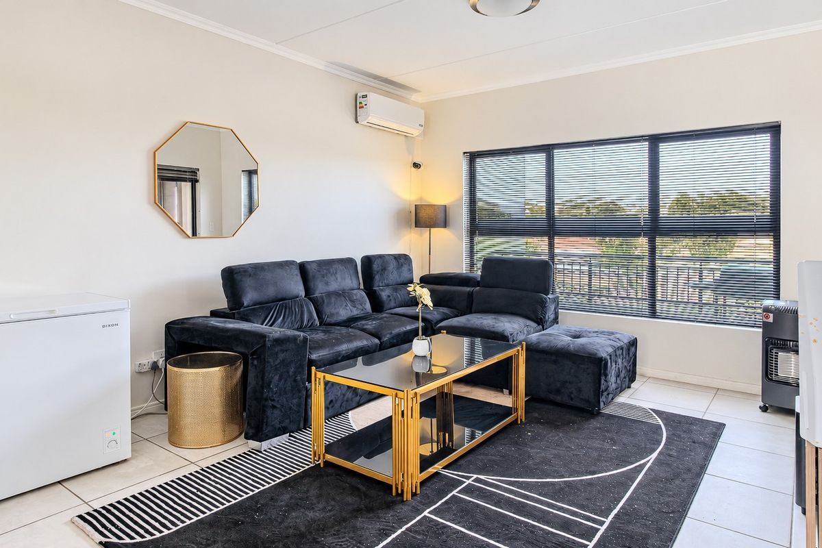 A bright and well-maintained living room featuring tiled flooring, a split-system air conditioner, and a large window with fitted blinds.