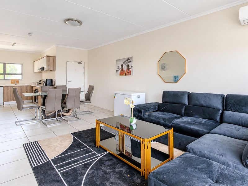 Spacious open-plan living and dining area featuring tiled floors, a modern kitchen with built-in cabinetry, and a wall-mounted air conditioning unit.