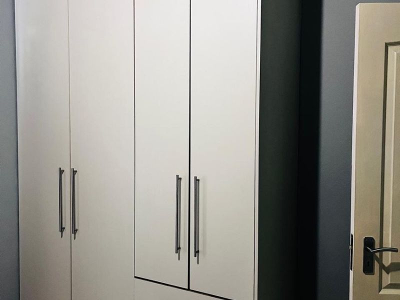 A bedroom featuring a modern, white built-in wardrobe with integrated drawers and sleek metal handles.