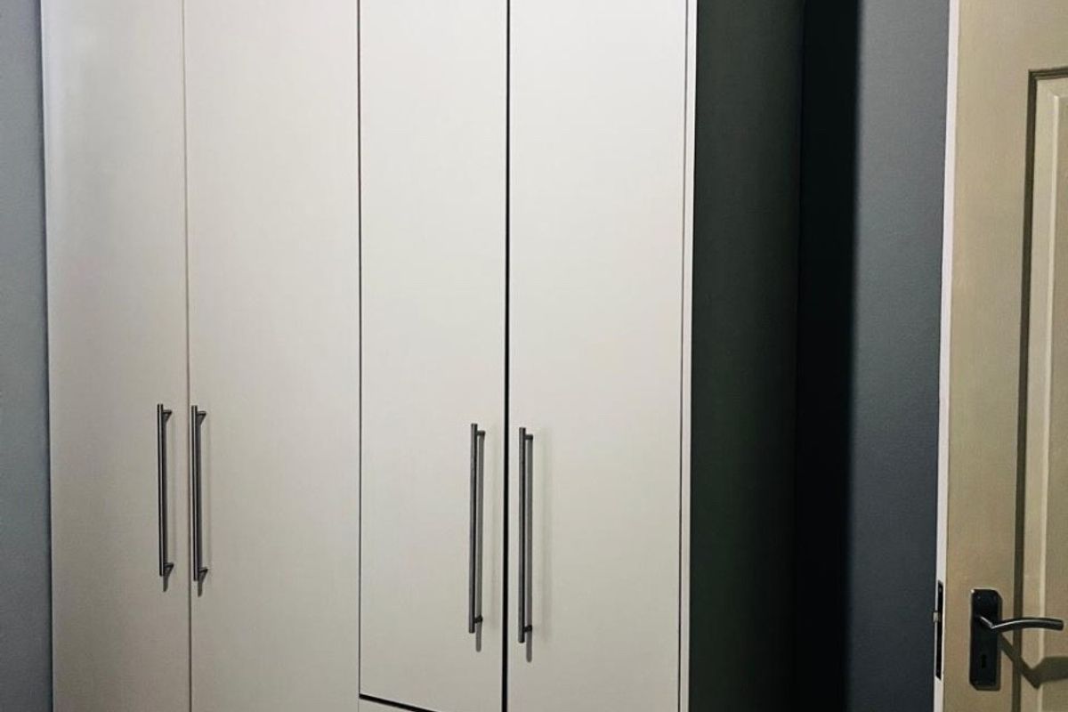 A bedroom featuring a modern, white built-in wardrobe with integrated drawers and sleek metal handles.