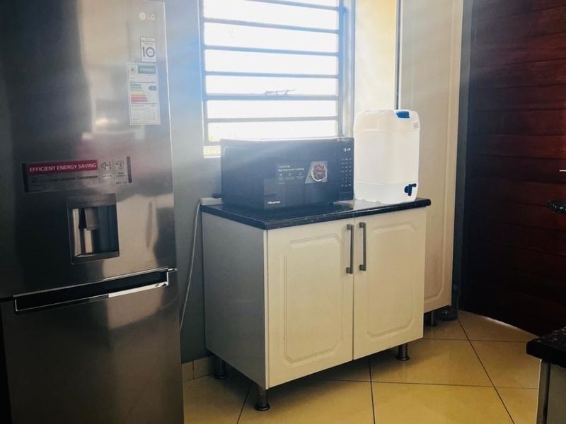 A functional kitchen area featuring tiled flooring, white built-in cabinetry with granite countertops, and a louvered window for natural light.