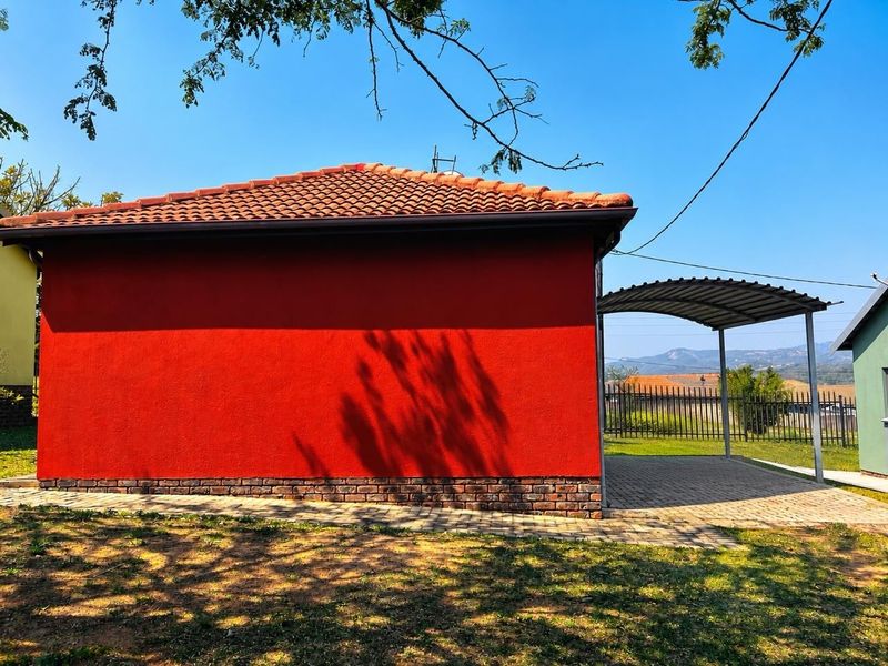 Rear view of the property featuring a red rendered facade, tiled roof, and a covered carport area with paved driveway.