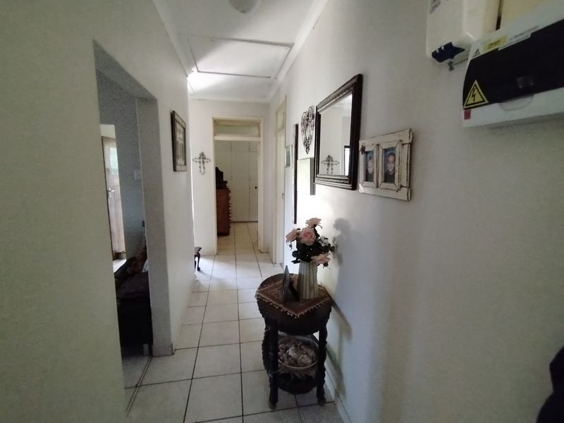 A functional residential hallway featuring tiled flooring, a ceiling access hatch, and a wall-mounted electrical distribution board.