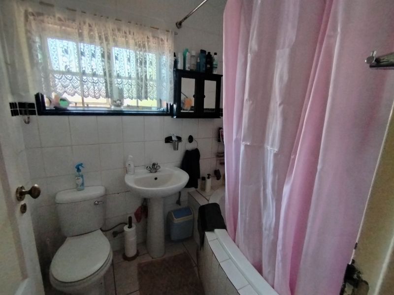 A functional bathroom featuring a pedestal basin, toilet, and a bathtub with a shower curtain, finished with white wall tiles and floor tiling.