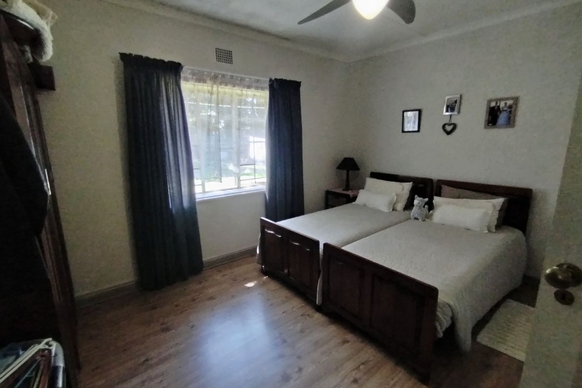 A functional bedroom featuring laminate flooring, a ceiling fan, and a window with curtains, providing a comfortable and well-lit living space.