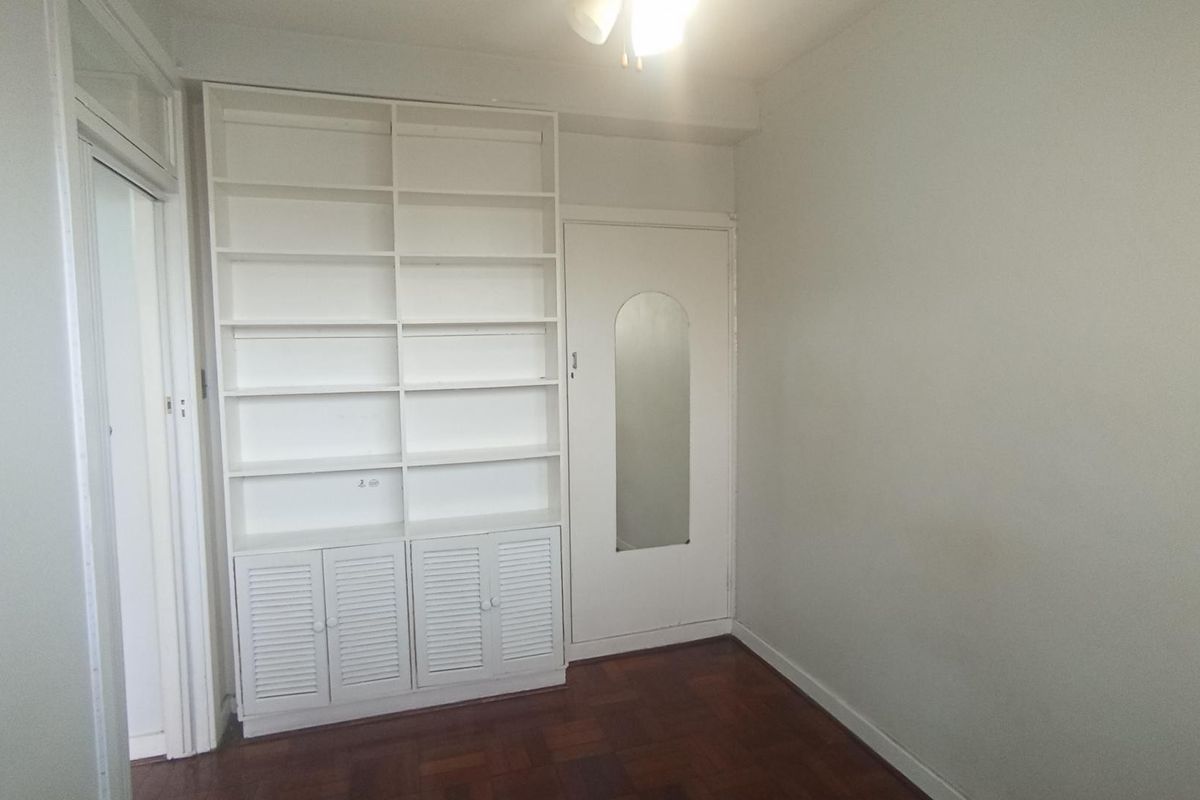 A vacant bedroom featuring parquet flooring, a large built-in shelving unit with lower storage cabinets, and an internal door with a mirror panel.