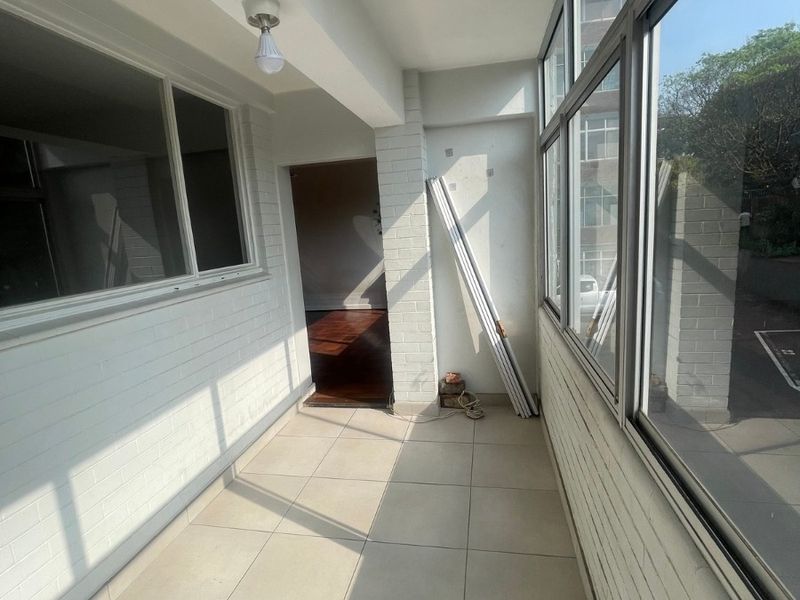A bright, enclosed balcony featuring tiled flooring, painted brick walls, and large windows, offering a versatile space for a sunroom or relaxation area.