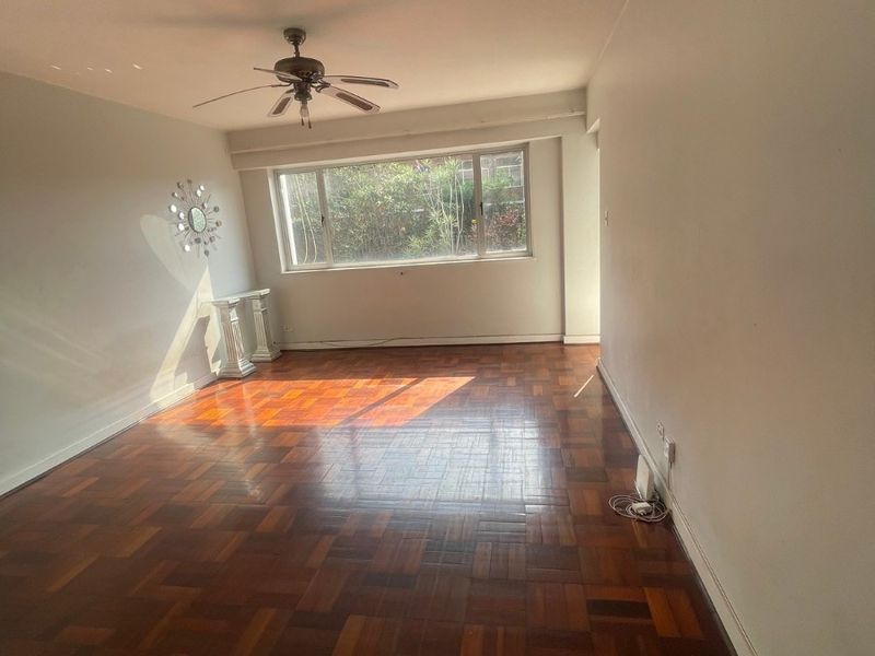 Spacious living area featuring classic parquet flooring and a ceiling fan, offering a bright and open space ready for personalization.