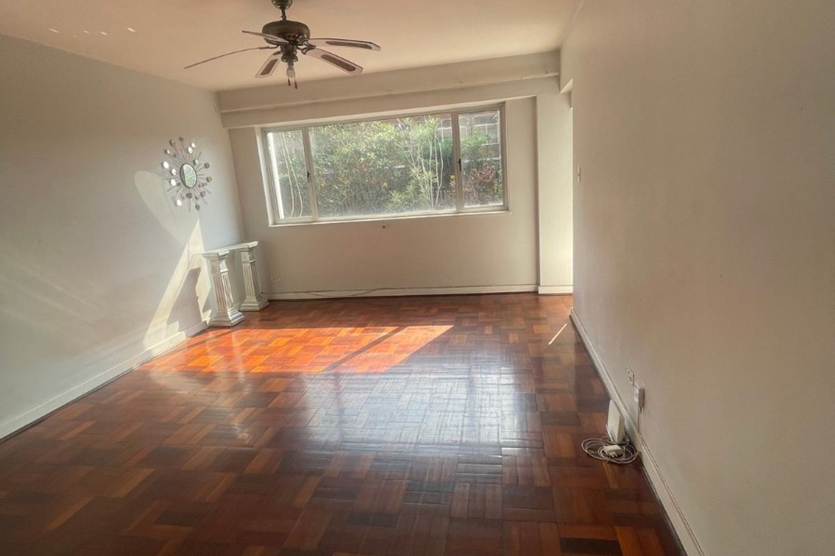 Spacious living area featuring classic parquet flooring and a ceiling fan, offering a bright and open space ready for personalization.