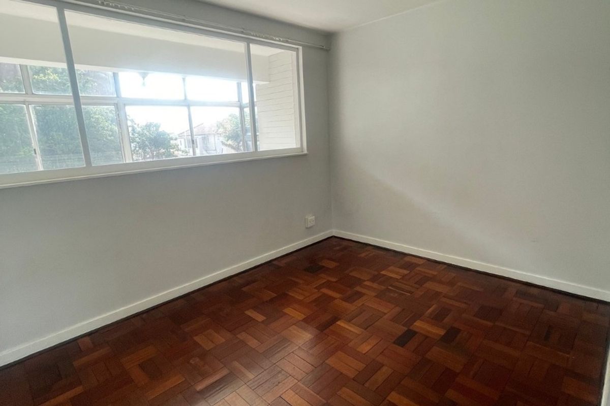A bright, empty bedroom featuring well-maintained parquet flooring, a ceiling fan, and large sliding windows providing natural light.