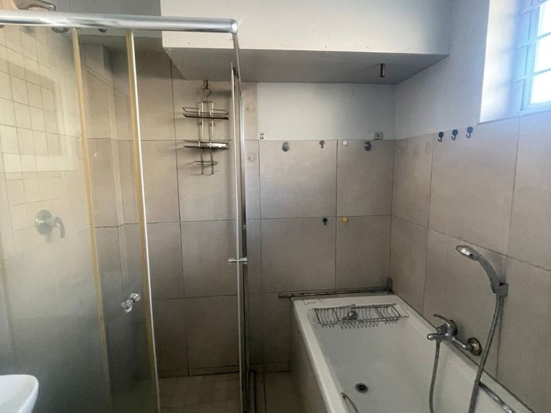 A functional bathroom featuring a separate shower enclosure and a bathtub with tiled finishes and natural light from a side window.