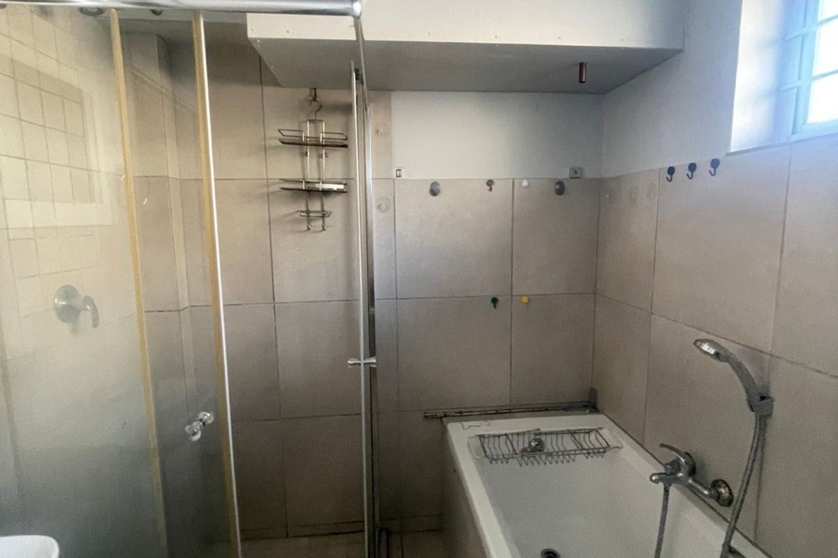 A functional bathroom featuring a separate shower enclosure and a bathtub with tiled finishes and natural light from a side window.