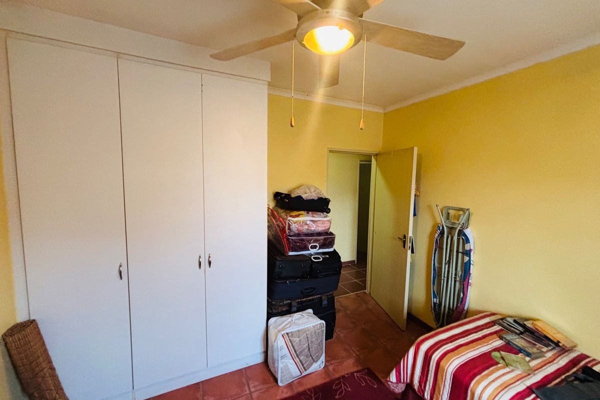 A bedroom featuring built-in wardrobes, a ceiling fan, and tiled flooring, offering a functional space with potential for cosmetic updates.