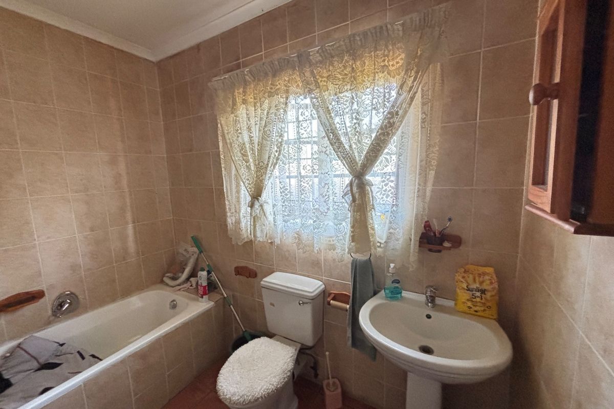 A functional bathroom featuring a bathtub, pedestal washbasin, and toilet with neutral wall and floor tiling.