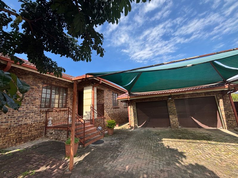 Front exterior view featuring a face brick facade, double garage with roll-up doors, and a shade cloth carport over a paved driveway.
