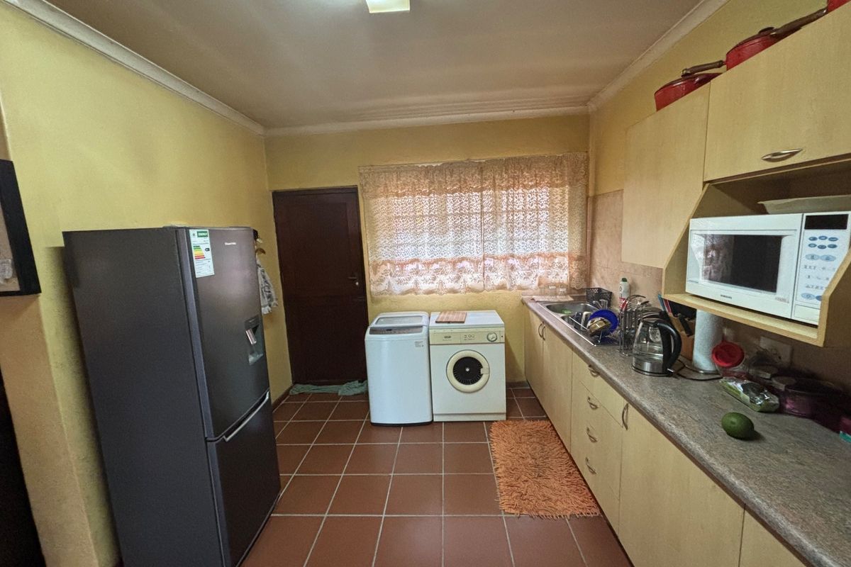 Functional kitchen featuring built-in cabinetry, laminate countertops, and tiled flooring, providing a practical layout with space for laundry appliances.