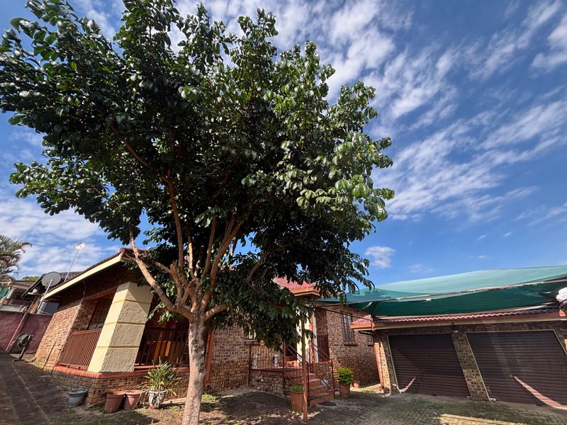 Front view of a face brick house featuring a double garage with roll-up doors, a shade cloth carport, and a covered entrance porch.