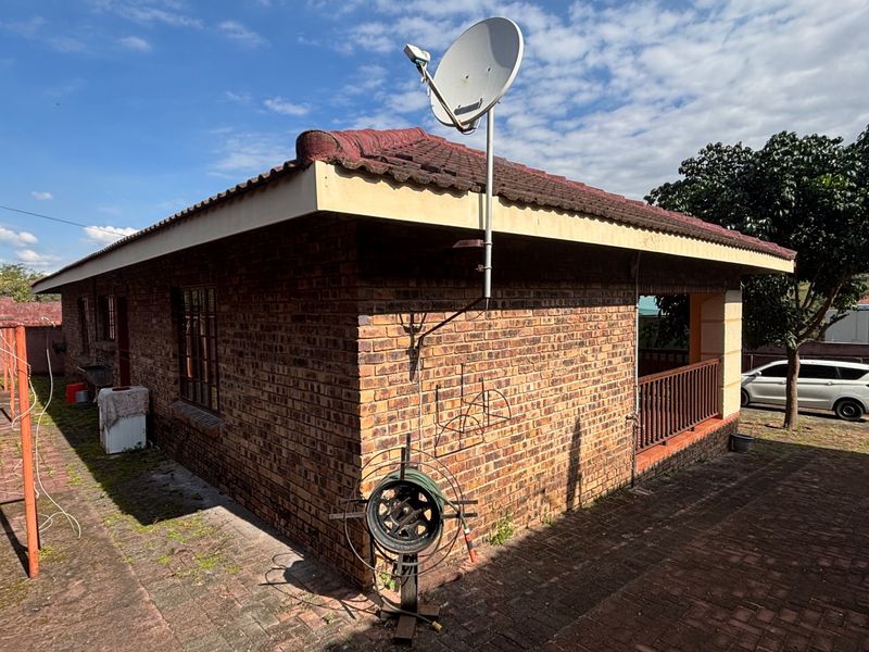 Rear view of a face brick house featuring a tiled roof, satellite dish, and a paved patio area with a railing.