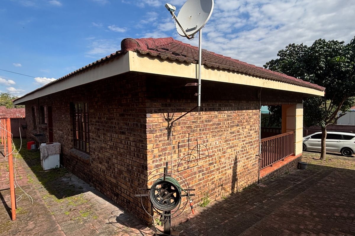 Rear view of a face brick house featuring a tiled roof, satellite dish, and a paved patio area with a railing.