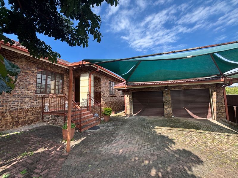 Front exterior view of a face brick house featuring a double garage, paved driveway, and a shade cloth carport structure.
