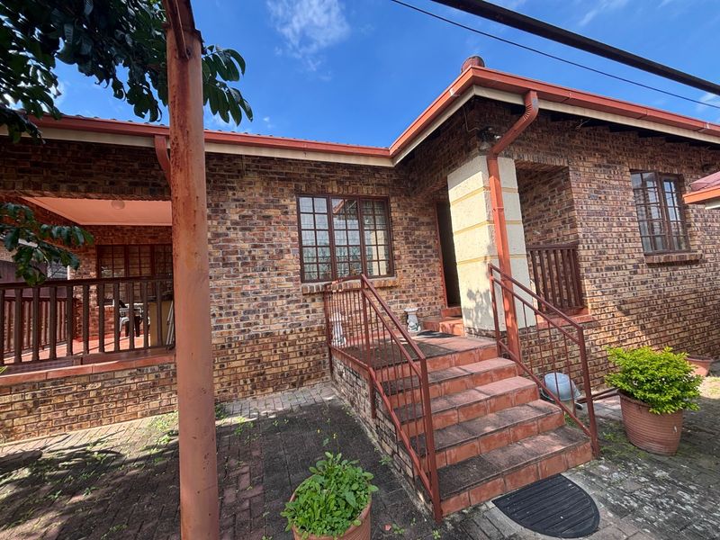 Rear exterior view of a face brick house featuring a covered patio, brick staircase with metal railings, and a paved courtyard area.
