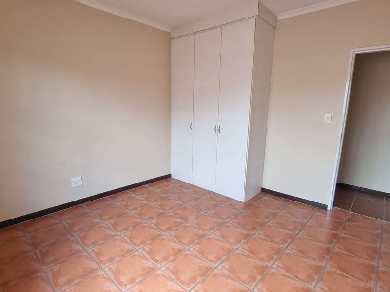 A clean, empty bedroom featuring neutral walls, tiled flooring, and a functional built-in wardrobe, offering a blank canvas for personalization.
