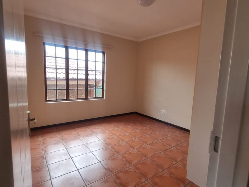 A vacant bedroom featuring terracotta-style floor tiles and a classic lattice window, offering a clean and neutral space ready for personalization.