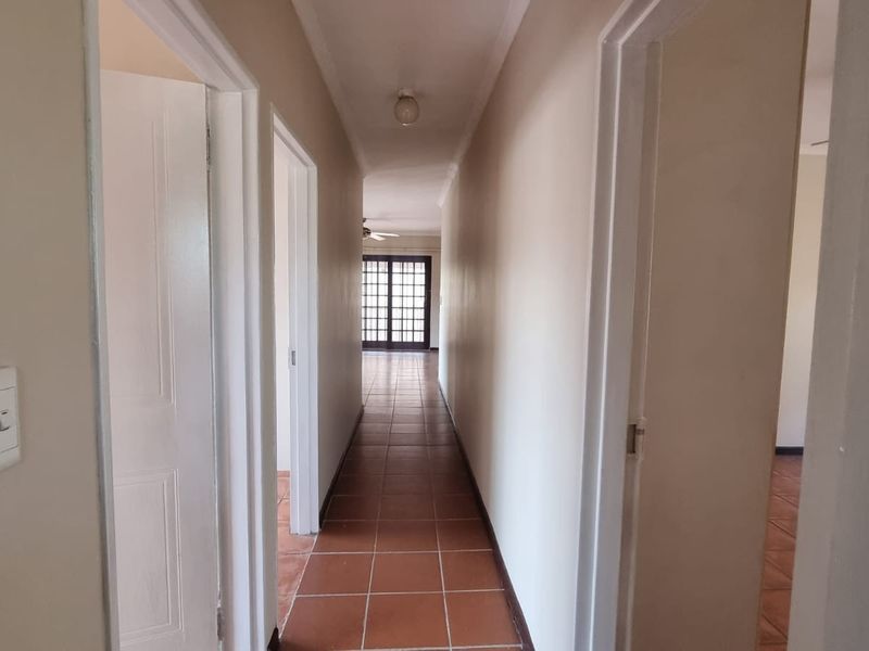 A clean, neutral hallway featuring tiled flooring and multiple internal access points, leading towards a bright living area with glass-paneled doors.
