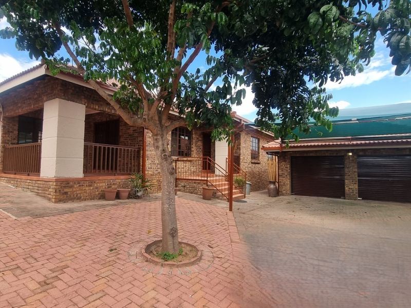 Front view of a face brick house featuring a paved driveway, double garage with shade cloth carport, and a covered entrance patio.