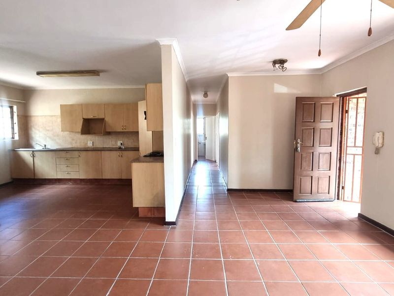Spacious open-plan living area featuring tiled flooring, built-in kitchen cabinetry, and direct access to the entrance, offering a functional layout ready for modernization.