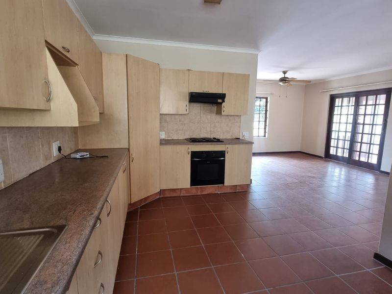 Spacious open-plan kitchen and living area featuring tiled flooring, built-in cabinetry, and direct access to the patio through classic french doors.