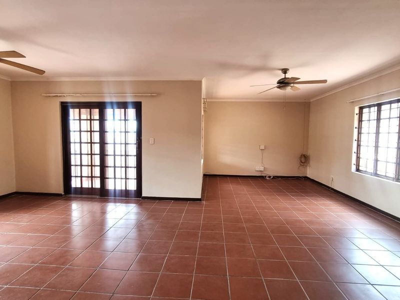 Spacious, open-plan living area featuring terracotta floor tiles, dual ceiling fans, and large sliding glass doors providing access to the exterior.