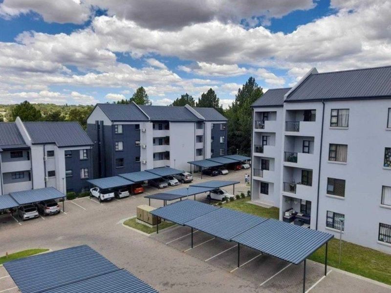 Aerial view of a modern apartment complex featuring multiple residential blocks, covered parking bays, and paved driveway areas.