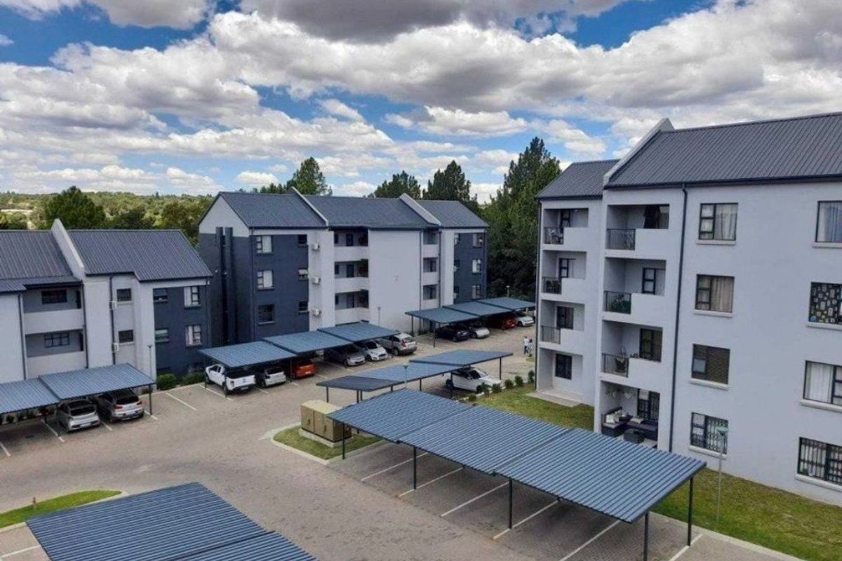 Aerial view of a modern apartment complex featuring multiple residential blocks, covered parking bays, and paved driveway areas.