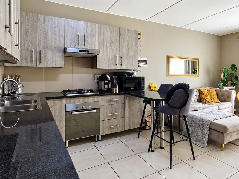 Open-plan living area featuring a modern kitchen with laminate cabinetry, granite countertops, gas hob, and tiled flooring, seamlessly flowing into the lounge space.