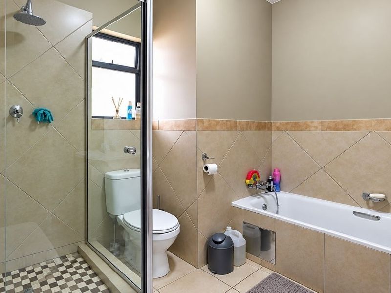 A well-maintained bathroom featuring a separate shower enclosure with a rain shower head, a bathtub, and neutral wall tiling.